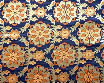 Könnte beinhalten: Ein Stoff mit einem sich wiederholenden Blumenmuster in Orange, Gold und Creme auf dunkelblauem Grund. Ein weißes Maßband liegt am unteren Rand und zeigt Maße von 10 bis 37 cm auf der Textiloberfläche an.