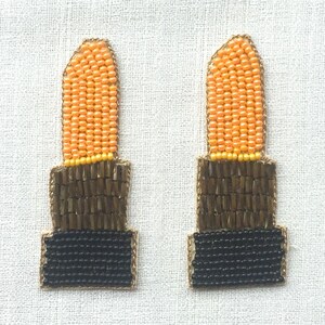 May include: Two beaded lipstick-shaped ornaments with orange, brown, and black beads.