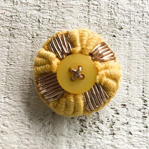 Peut inclure: Un bouton jaune avec des accents dorés et un bouton jaune au centre.