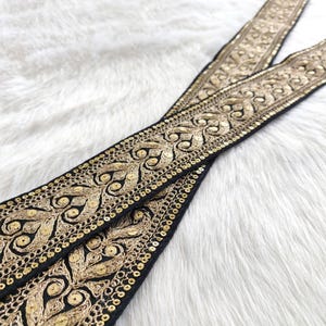 May include: Black trim with gold embroidery and sequins. The trim has a repeating pattern of floral designs.