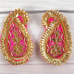 Può includere: Due ricami in tessuto rosa a forma di paisley con ricami dorati e arancioni e paillettes.