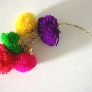 May include: A colorful keychain with four pom-poms in red, green, yellow, and purple. The pom-poms are attached to a gold chain.