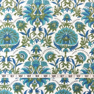 May include: White fabric with a repeating pattern of blue and green floral designs. The fabric is measured with a ruler in inches.