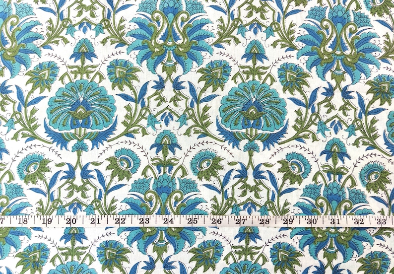 May include: White fabric with a repeating pattern of blue and green floral designs. The fabric is measured with a ruler in inches.