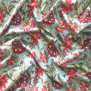 May include: A teal fabric with a red and green floral print. The fabric is folded and has a wrinkled texture.