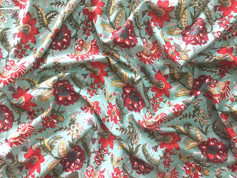 May include: A teal fabric with a red and green floral print. The fabric is folded and has a wrinkled texture.