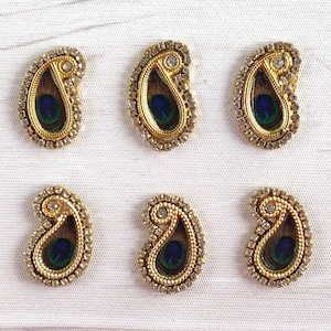 Puede incluir: Seis adornos dorados y blancos en forma de paisley con un diseño de pluma de pavo real. Los adornos son perfectos para agregar un toque de elegancia a cualquier proyecto artesanal.