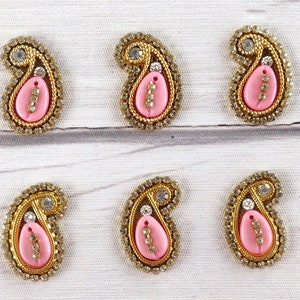 May include: Six gold paisley-shaped embellishments with pink centres and clear rhinestone accents.