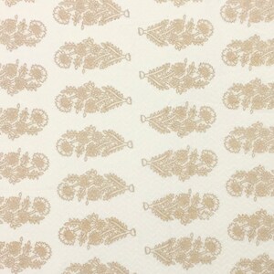 May include: White fabric with a repeating pattern of brown floral designs. The design is a stylized floral motif with a long, narrow shape.