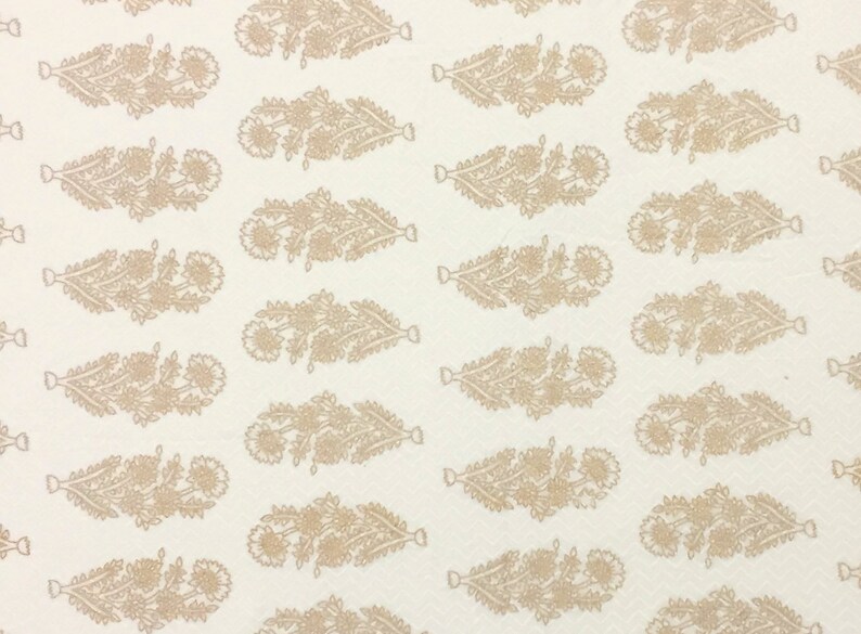May include: White fabric with a repeating pattern of brown floral designs. The design is a stylized floral motif with a long, narrow shape.
