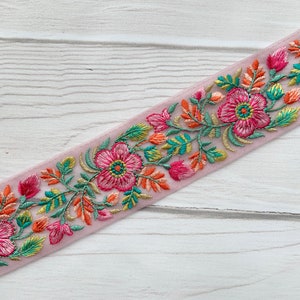 Op de afbeelding: Roze geborduurde bies met bloemenmotieven in tinten roze, groen, oranje en turquoise.