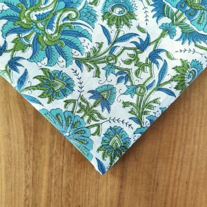 May include: A white fabric with a blue and green floral pattern. The fabric is folded in a triangle shape and the pattern is visible on both sides of the fold.