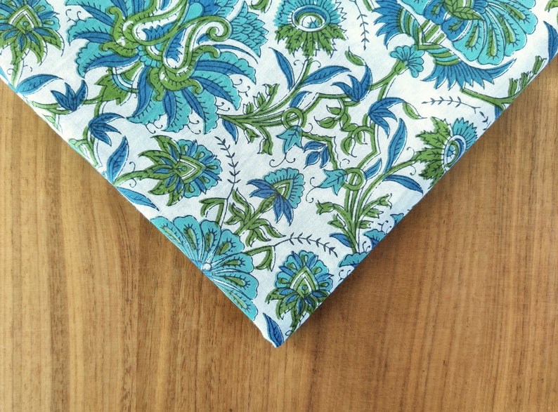 May include: A white fabric with a blue and green floral pattern. The fabric is folded in a triangle shape and the pattern is visible on both sides of the fold.