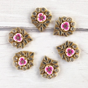 May include: Six gold-toned metal embellishments with pink flower accents and clear rhinestones. Each embellishment is shaped like a teardrop with a pointed tip.