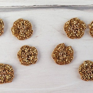 以下が含まれることがあります： ビーズのデザインが施された、金色の花の形をした装飾品が10個あります。