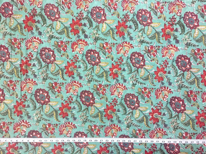 May include: Teal fabric with a repeating floral pattern. The flowers are red, burgundy, and yellow with green leaves. The fabric is measured in inches.