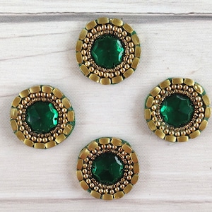 May include: Four round green and gold embellishments with a green gem in the centre. The embellishments are perfect for adding a touch of sparkle to crafts and clothing.