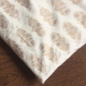 May include: White fabric with a gold floral pattern. The fabric is folded in half and the pattern is visible on both sides.