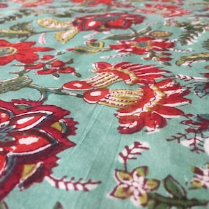 May include: A teal fabric with a red and green floral print. The fabric features a repeating pattern of flowers and leaves.