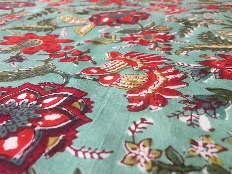 May include: A teal fabric with a red and green floral print. The fabric features a repeating pattern of flowers and leaves.