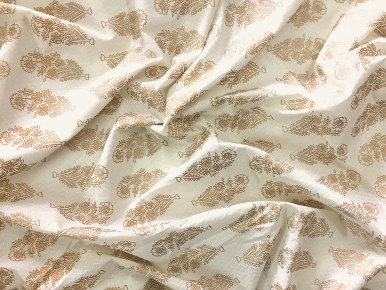 May include: White fabric with a gold floral pattern. The fabric is wrinkled and has a soft, textured surface.