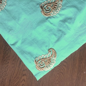 May include: A turquoise fabric with gold and white paisley embroidery.