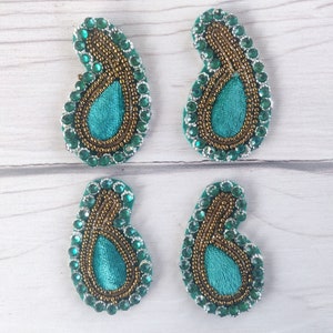 May include: Four teal blue paisley shaped fabric patches with gold and green bead embellishments.