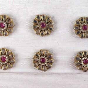 May include: Six gold-toned metal flower-shaped embellishments with clear and pink rhinestones. Each embellishment has a central pink rhinestone surrounded by clear rhinestones.
