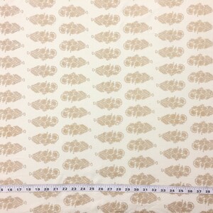 May include: White fabric with a repeating pattern of beige stylized floral sprigs. The fabric has a ruler with inch markings at the bottom.