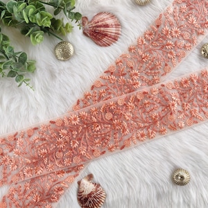 Puede incluir: Borde de encaje de color melocotón con un diseño floral. El borde está hecho de una tela transparente y tiene un aspecto delicado y femenino.