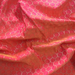 Pode incluir: Um close-up de um tecido rosa com um padrão de favo de mel dourado. O tecido está enrugado e tem uma sensação macia e texturizada.