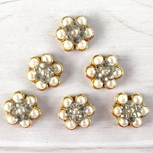 May include: Six gold-colored flower-shaped embellishments with white pearl-like beads and clear rhinestones.