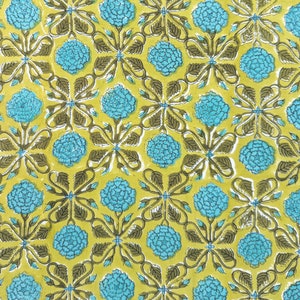 May include: Close-up of a fabric with a repeating floral pattern. The design features turquoise blue flower clusters and dark olive green leaves and stems on a yellow-green background. The pattern is symmetrical and detailed.