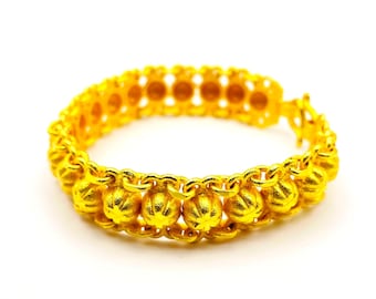 Könnte beinhalten: Ein goldfarbenes Armband mit einem sich wiederholenden Muster aus kleinen, runden, strukturierten Perlen. Das Armband besteht aus einem glänzenden, metallischen Material und ist vor einem weißen Hintergrund platziert. Das Armband hat einen Umfang von etwa 18 cm.