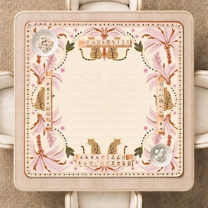 Può includere: Un tappetino da mahjong quadrato con un centro color crema bordato da foglie di palma rosa, fogliame verde e illustrazioni di leopardi. Quattro supporti in legno per tessere sono posizionati lungo i bordi, ciascuno con tessere con simboli.