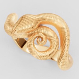 May include: A gold ring featuring a textured snake design. The snake's body wraps around the finger, with the head and tail forming a spiral. The ring is made of a shiny, metallic material.