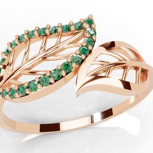 Puede incluir: Anillo de oro rosa con diseño de hoja calada. La hoja está adornada con pequeñas piedras preciosas verdes redondas. La banda del anillo se curva con gracia, creando una pieza de joyería elegante e inspirada en la naturaleza.