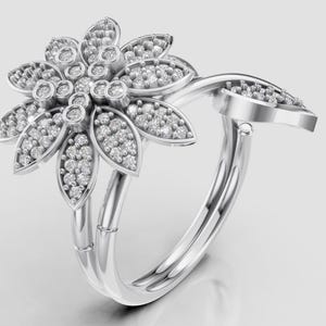 Può includere: Un anello color argento con un design floreale. Il fiore ha più petali, ognuno incastonato con piccole gemme scintillanti. La fascia si curva con grazia, aggiungendo all'aspetto elegante dell'anello. L'anello è un gioiello.