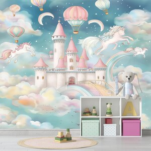 Op de afbeelding: Een grillige muurschildering met een sprookjeskasteel met roze torentjes, eenhoorns en luchtballonnen tegen een pastelkleurige lucht. Een witte plank bevat speelgoed en opbergdozen.