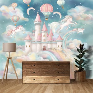 Op de afbeelding: Een sprookjesachtige muurschildering met een kasteel met roze torens, eenhoorns, luchtballonnen en een regenboog. De sc&egrave;ne speelt zich af tegen een dromerige lucht met wolken en sterren. Een houten dressoir met drie lades staat eronder.