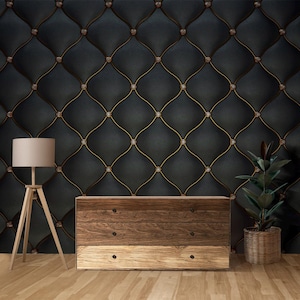 May include: Interior scene with a dark, quilted wall with a diamond pattern and gold detailing. A wooden chest of drawers and a floor lamp with a beige lampshade are in front of the wall. A potted plant is on the right.