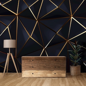 Puede incluir: Un interior moderno con una pared geométrica azul oscuro con detalles dorados. Una cómoda de madera con tres cajones, una lámpara de pie con una pantalla beige y una planta en maceta están frente a la pared. Suelo de madera.