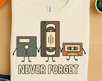 May include: Cream-colored sweatshirt featuring a graphic of a floppy disk, VHS tape, and cassette tape with arms and legs, holding hands. The text "NEVER FORGET" is printed below the graphic.