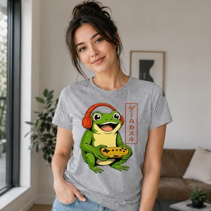 Op de afbeelding: Een grijs gemêleerd t-shirt met een afbeelding van een groene kikker met een oranje koptelefoon die een gele videogamecontroller vasthoudt. Rechts van de kikker staat een verticaal rood rechthoekig kader met de Japanse tekst ゲームカエル.
