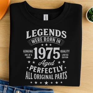 Puede incluir: Camiseta negra con texto blanco que dice "LEGENDS WERE BORN IN 1975". El texto también incluye "Genuine, One of a Kind, Aged, Perfectly, All Original Parts". La camiseta es de edición limitada.