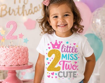 May include: A white short-sleeved t-shirt featuring a graphic print with a gold glitter number 2, a pink crown, and the text little MISS Two CUTE in pink, blue, and silver glitter. The shirt is worn with blue denim jeans and a pink hair bow.