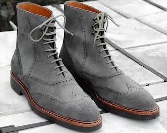 May include: A pair of gray suede leather boots with a lace-up design. The boots have a wingtip style with decorative perforations and a brown sole. The boots are approximately 6 inches tall.