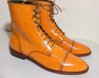 May include: A pair of bright orange leather boots with a glossy finish. The boots have a lace-up design with brown laces and eyelets. The soles are brown, and the boots have a classic, polished look.