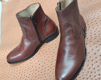 May include: Two brown leather ankle boots with black zippers. The boots have a classic design with a rounded toe and a low heel. The leather has a polished finish.