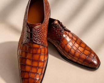May include: A pair of brown leather dress shoes featuring a prominent embossed crocodile skin texture. The shoes have a polished finish, a rounded toe, and thin dark brown laces. The design includes a distinct paneling detail on the upper.